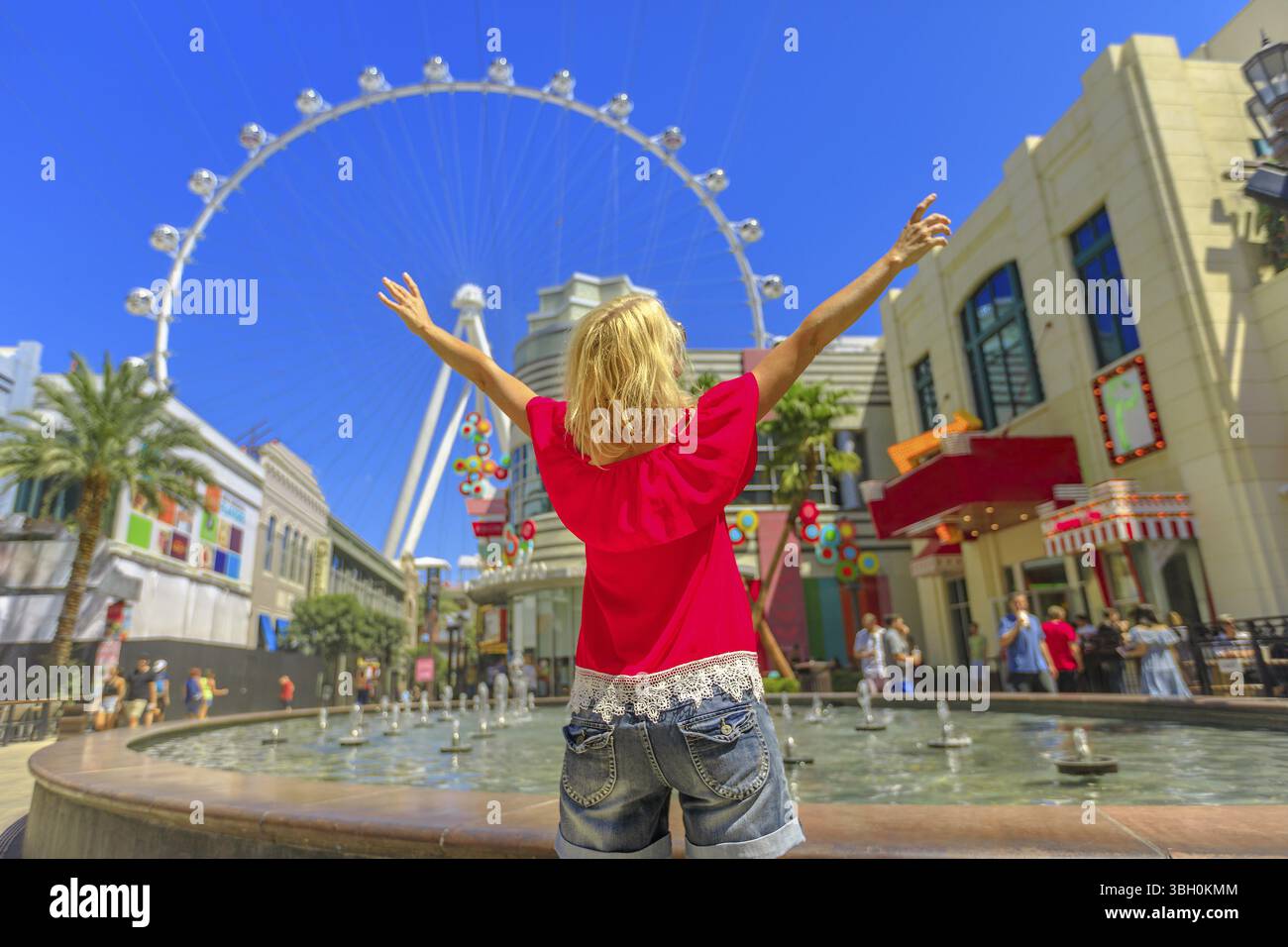 Donna bionda con le braccia alzate che guarda alla ruota panoramica, la ruota panoramica più grande del mondo al centro della Strip di Las Vegas. Buon turista al Las Vegas cit Foto Stock