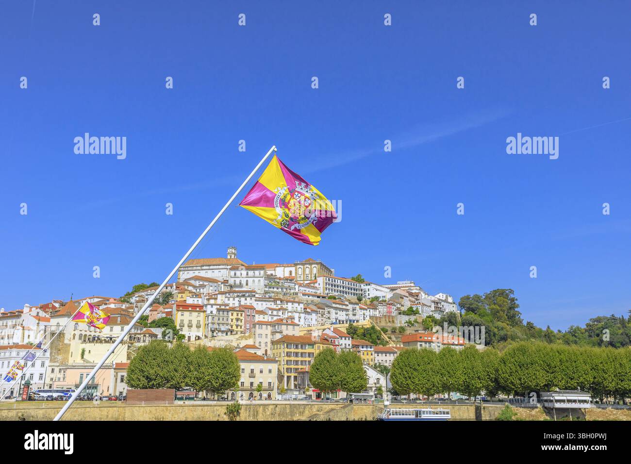Vista panoramica della città vecchia di Coimbra e del fiume Mondego dal ponte di Santa Clara con la bandiera di Coimbra che sventola in primo piano Foto Stock