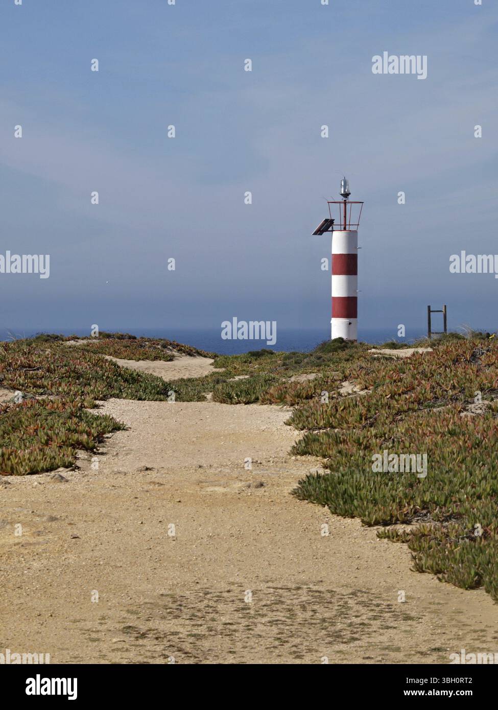 Tipico paesaggio di dune sulla costa dell'Alentejo con faro rosso e bianco Foto Stock