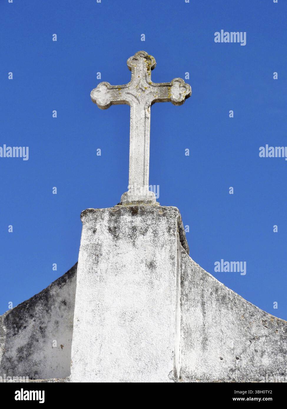Guglia della chiesa con croce di pietra di fronte a un cielo blu Foto Stock