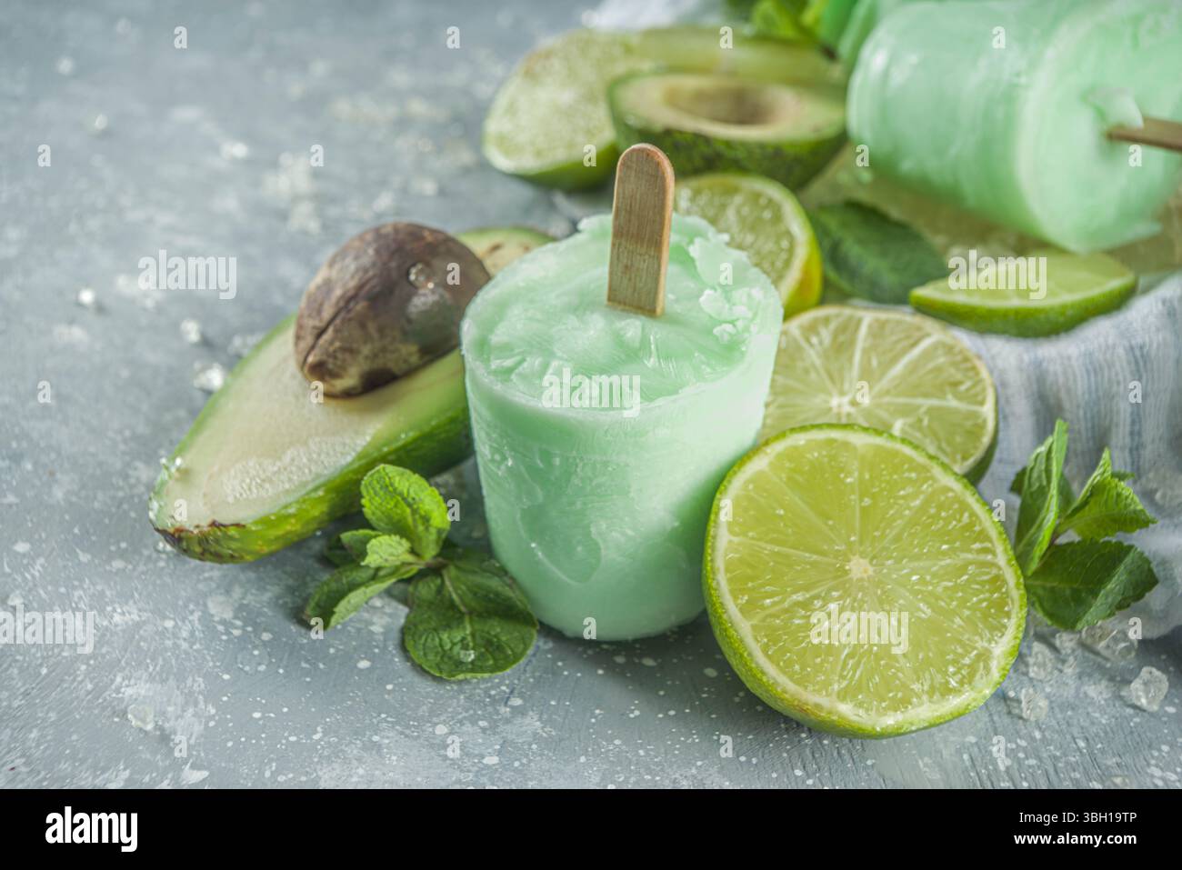 Papsicle avocado fatti in casa. Gelato vegano non caseario. Avocado, lime e cocco papsicle sano su sfondo grigio pietra con fette di calce fresca, avoca Foto Stock