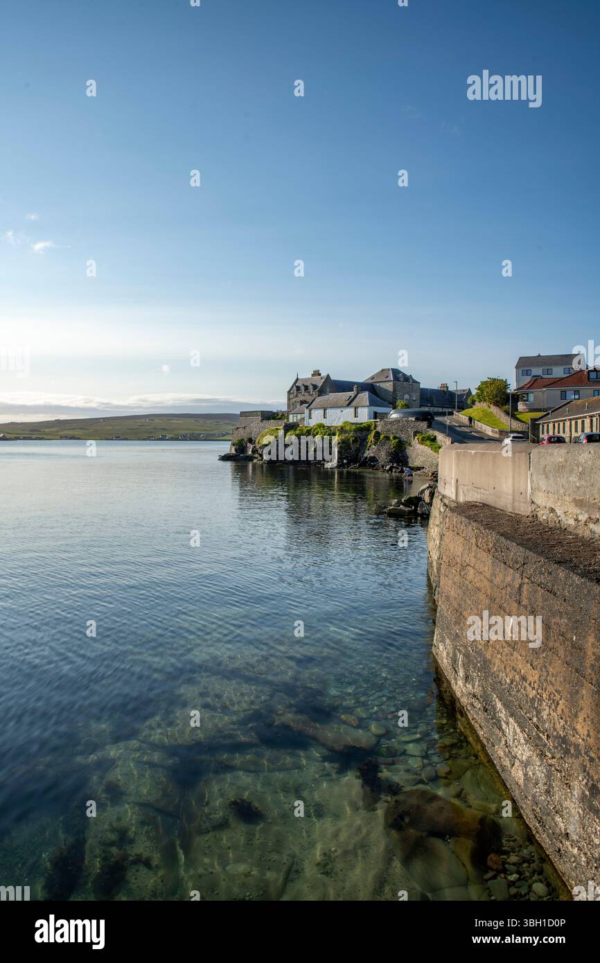 Ingresso sud al porto di Lerwick, Shetland, proprietà costiere in una tranquilla luce estiva con mare tranquillo e cieli blu. Foto Stock