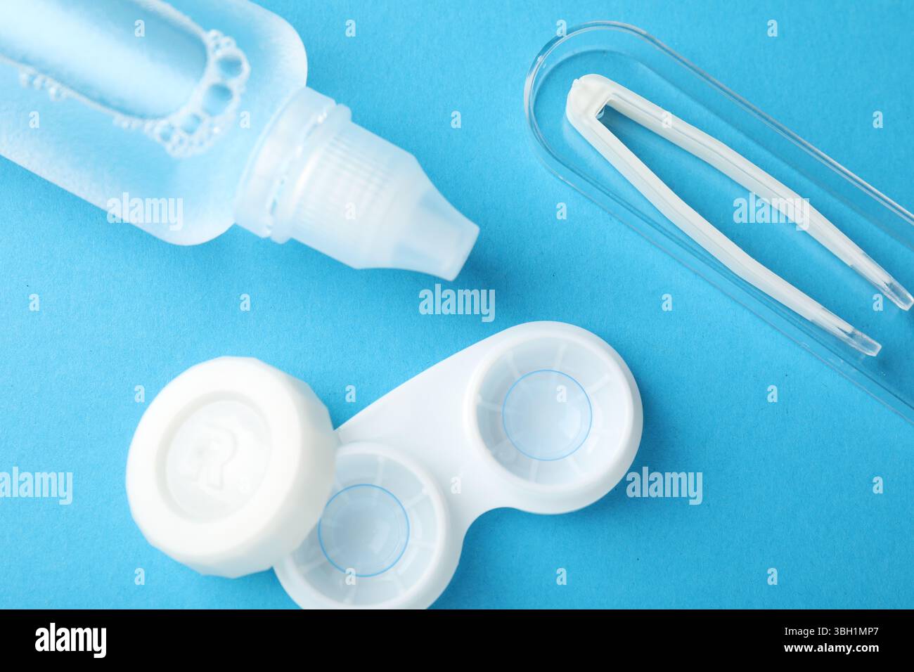 Lenti a contatto in astuccio, soluzione e pinzette su sfondo blu, posizione piatta Foto Stock