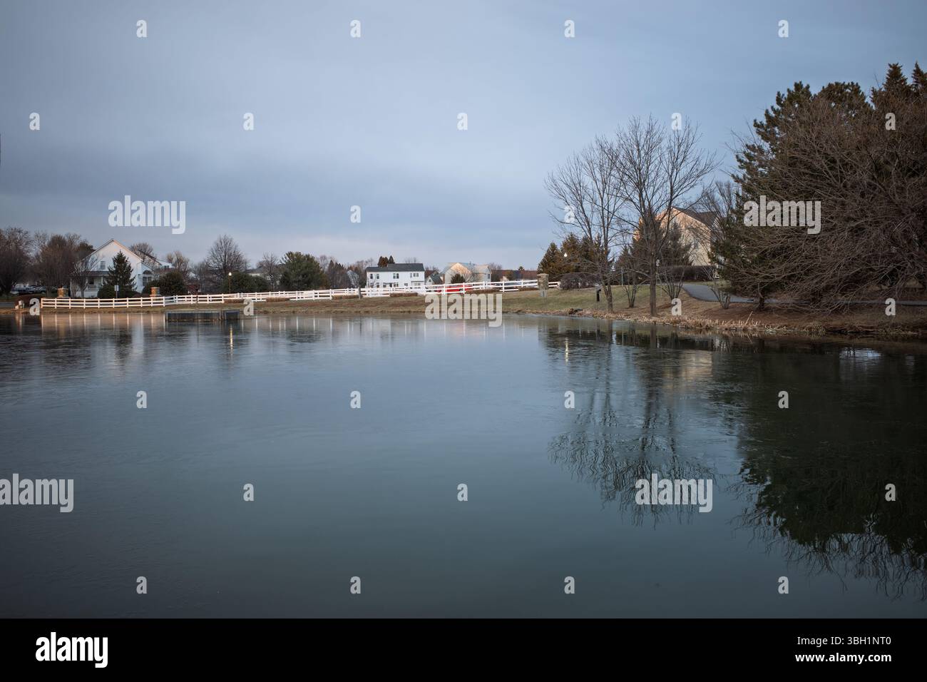 Un fresco mattino presto ad Ashburn, Virginia, rivela un tranquillo laghetto residenziale parzialmente congelato, che riflette la tranquilla bellezza dell'inverno sotto il soffice m Foto Stock