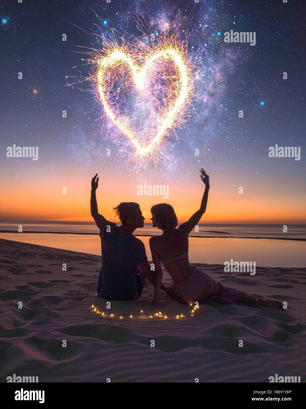 Giovane coppia innamorata seduta davanti a una spettacolare vista del tramonto sul mare, guardando i fuochi d'artificio e baciandosi a vicenda. Amore, concetto di relazione Foto Stock