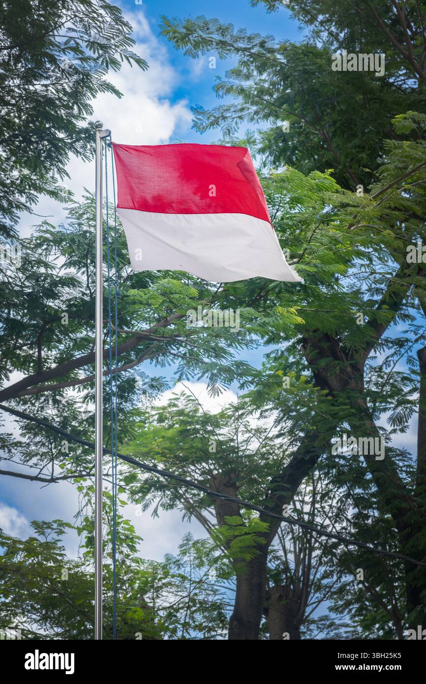 La bandiera rossa e bianca sta sventolando in aria. La bandiera è su un palo e quella è la bandiera indonesiana Foto Stock