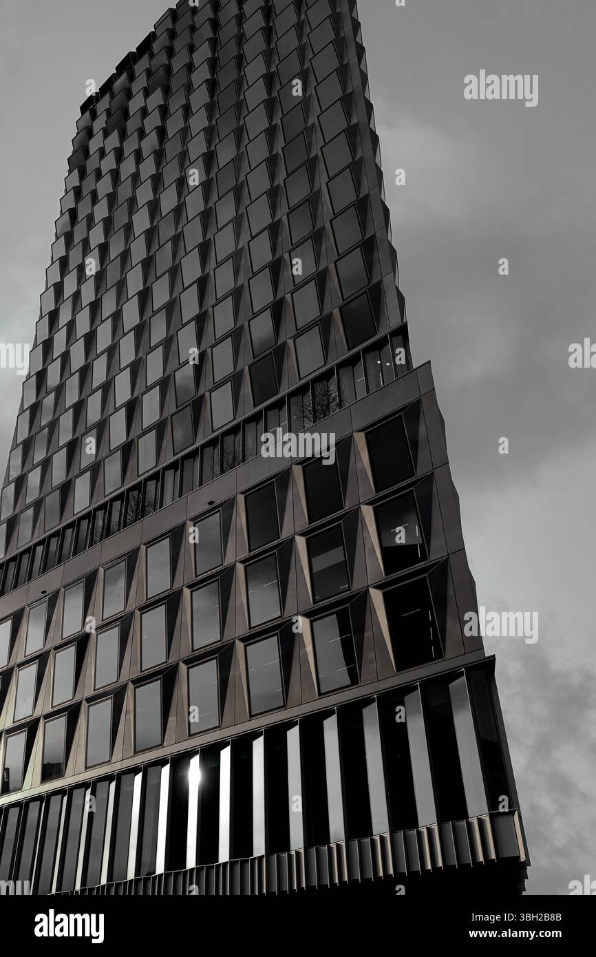 La torre Pulse si infila sotto nuvole di nuvole nella Zuidas di Amsterdam, con una facciata in vetro e metallo che riflette l'elegante architettura moderna, la vivacità e la vita urbana. Foto Stock