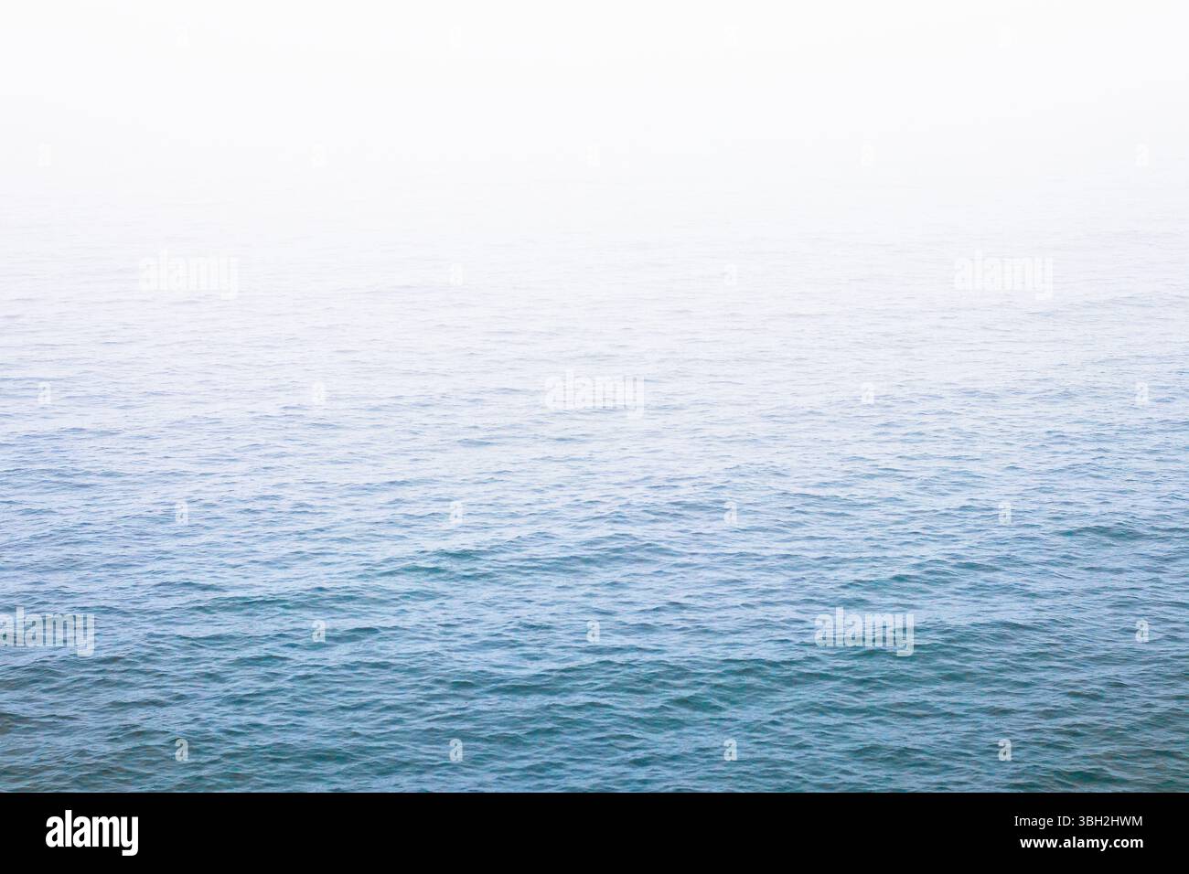 Le morbide onde blu svaniscono in un luminoso orizzonte nebbioso lungo la costa del Pacifico a Oceanside, California. Calmo e minimo, ideale per gli sfondi o per il relax Foto Stock