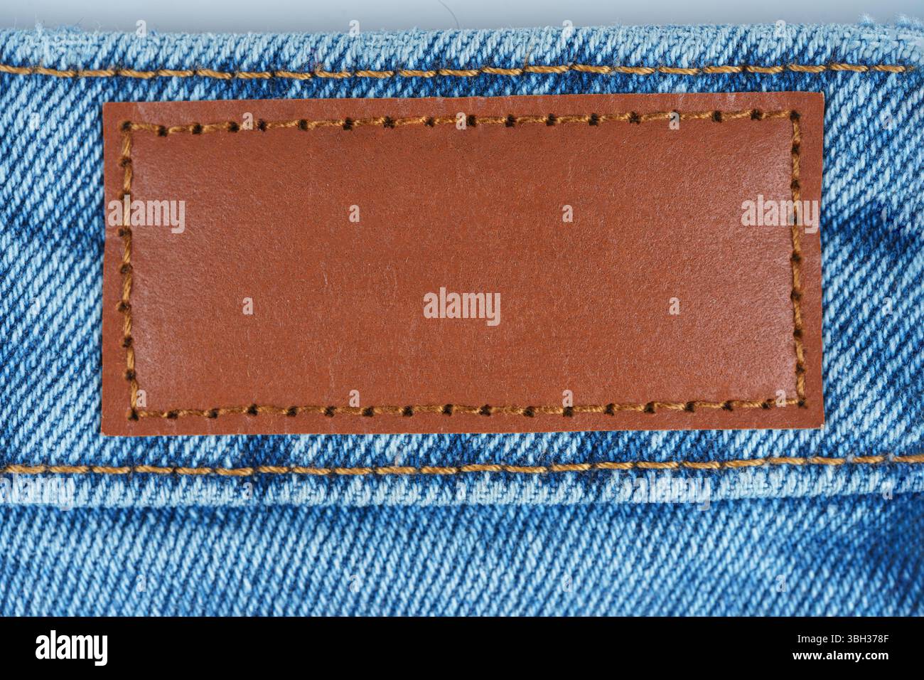 Primo piano dell'etichetta marrone in pelle cucita su jeans blu denim. Texture macro del tessuto e cuciture. Ideale per concetti di moda, tessile o branding negli annunci Foto Stock