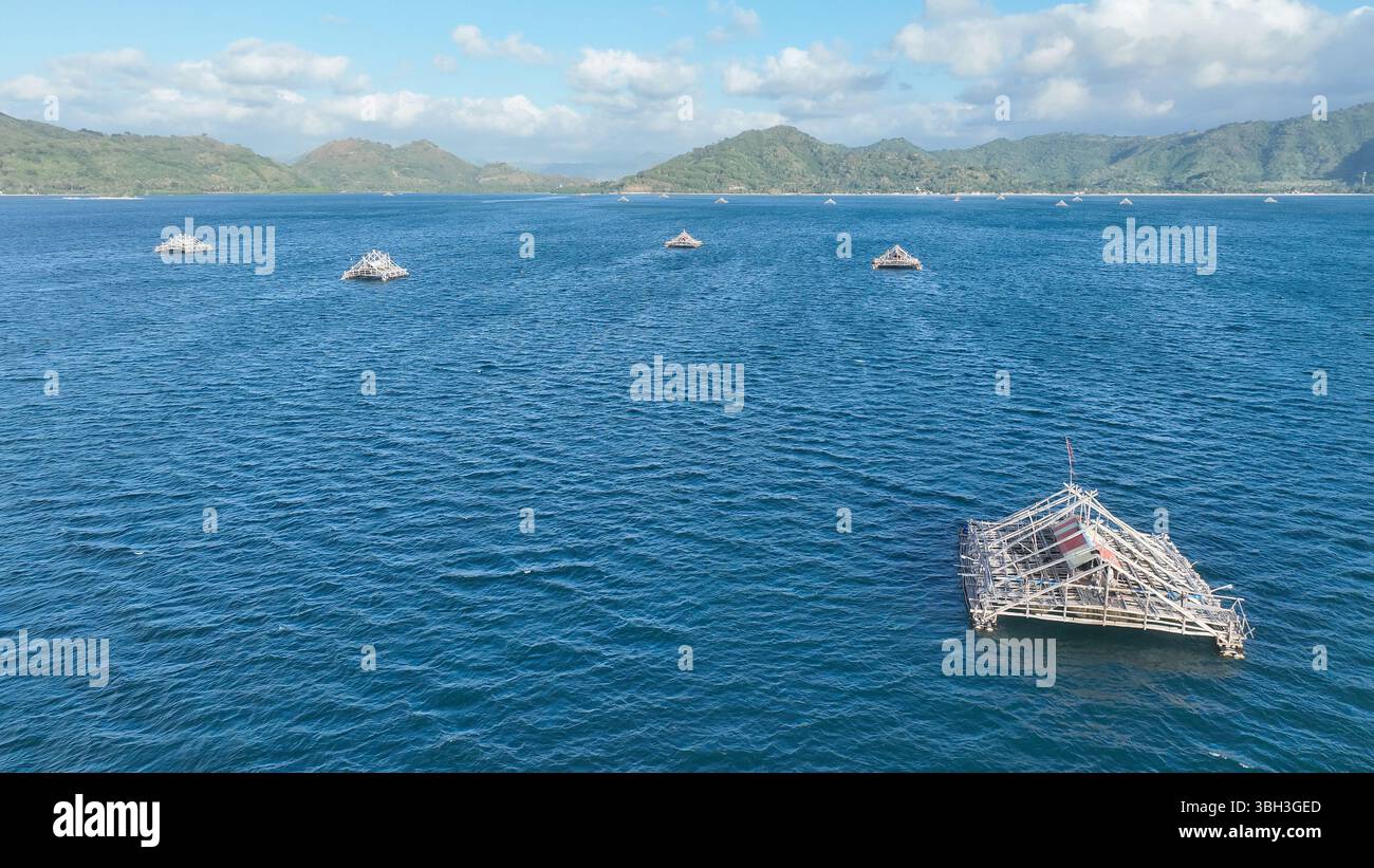 Le tradizionali piattaforme di pesca di bambù galleggiano sul mare blu vicino a Lombok. La vista aerea cattura le strutture uniche con lussureggianti colline verdi nel Foto Stock