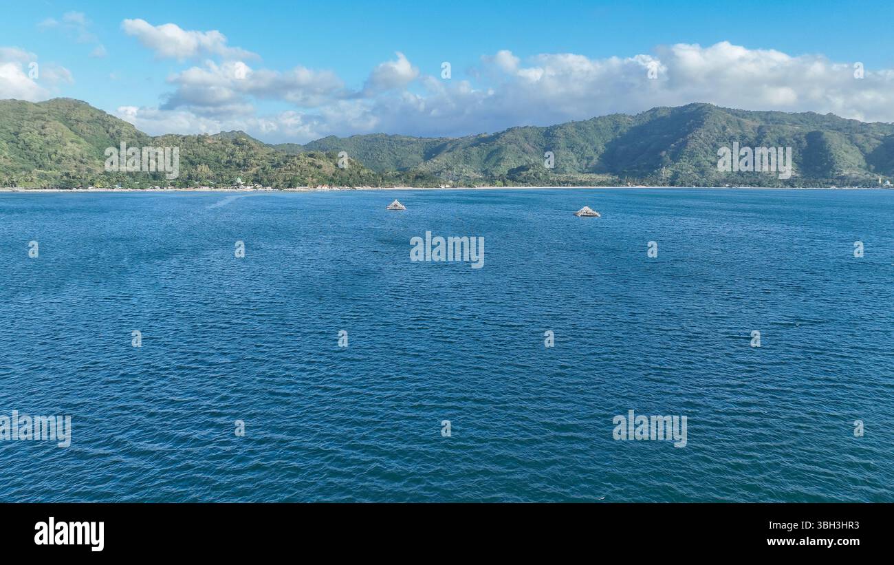 Il mare cristallino si estende fino all'orizzonte con due piattaforme di pesca in bambù, incorniciate da spettacolari montagne verdi e da un cielo blu vibrante sparso Foto Stock