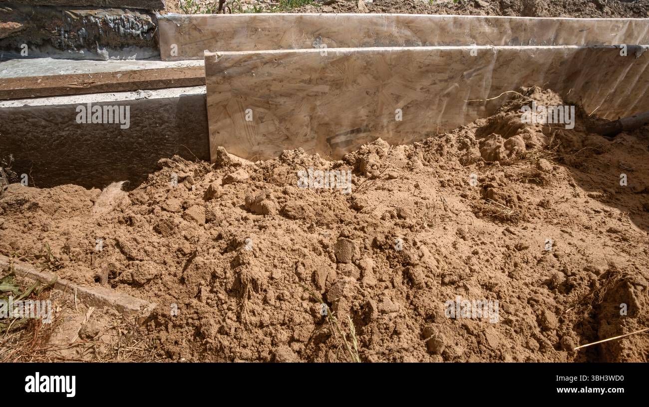 Primo piano di casseforme di fondazione e pareti in calcestruzzo impermeabili nel cantiere. Sabbia e materiali da costruzione visibili. Foto Stock