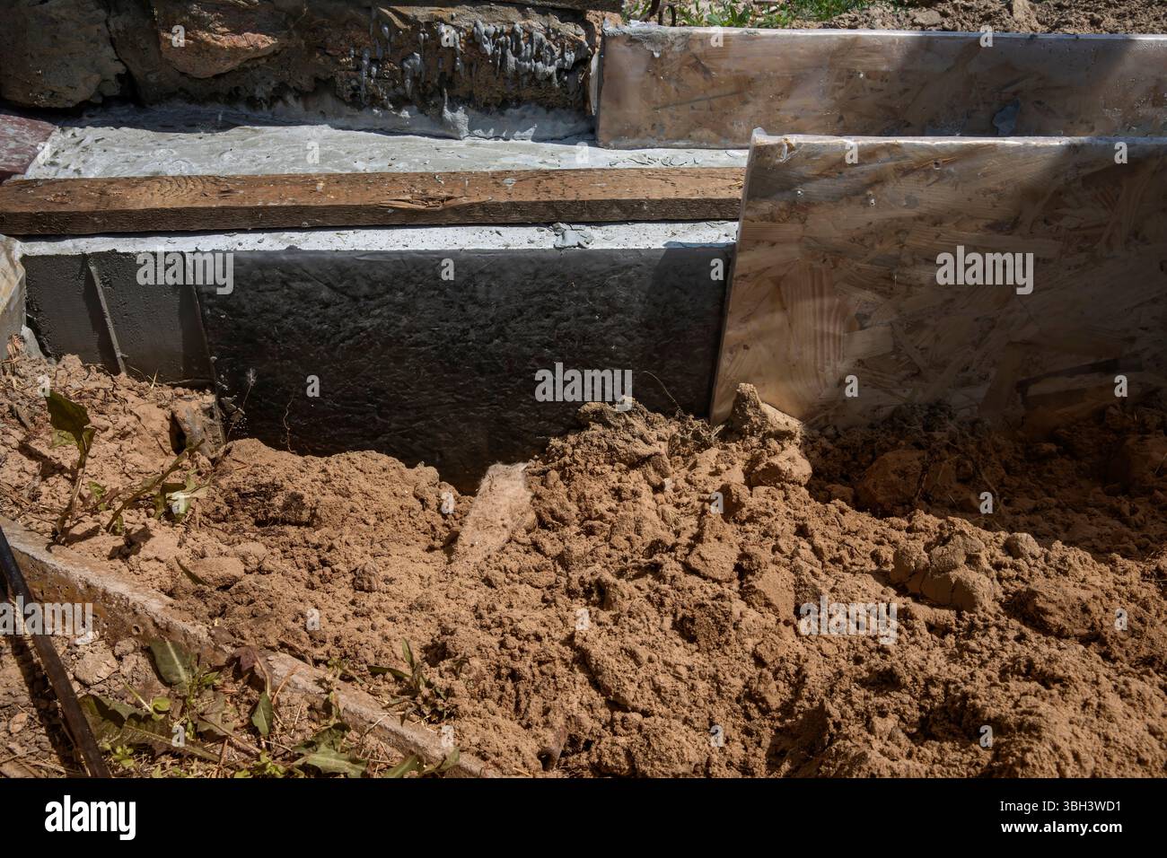 Primo piano di casseforme di fondazione e pareti in calcestruzzo impermeabili nel cantiere. Sabbia e materiali da costruzione visibili. Foto Stock