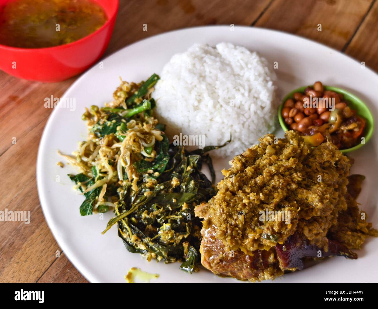 Un piatto di riso al pollo Betutu arrosto con pollo speziato, verdure saltate, germogli di soia, arachidi fritte, sambal, e zuppa di erbe speziate Foto Stock