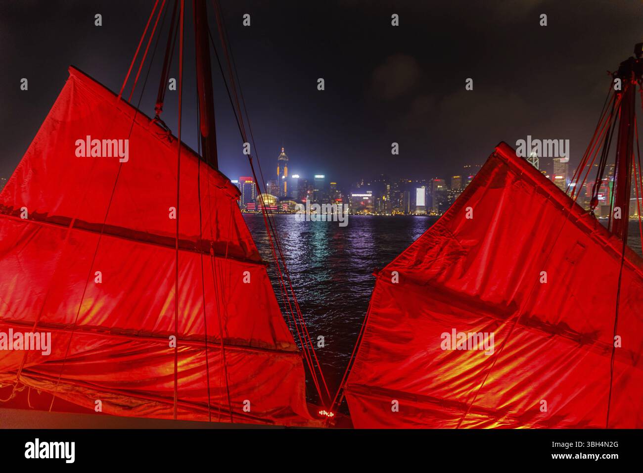 Primo piano di una junk boat a vela rossa con lo sfondo dello skyline dell'isola di Hong Kong visto dal lungomare di Tsim Sha Tsui a Kowloon Foto Stock