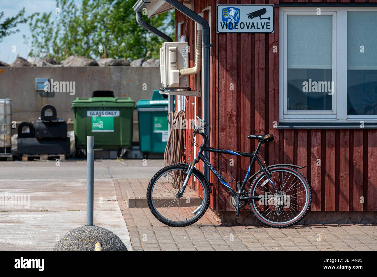 Ruhnu, Estonia - 1 giugno 2025: Una bicicletta si appoggia contro un edificio di legno rosso vicino a un'area portuale di Ruhnu, Estonia. Foto Stock