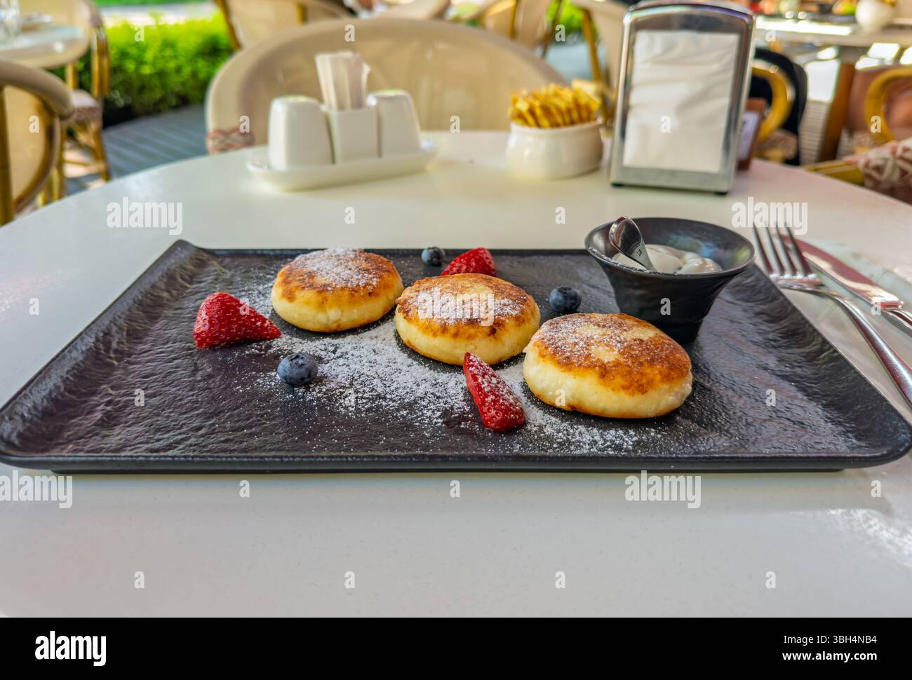 Sciroppi tradizionali, o frittelle di formaggio, serviti con frutti di bosco freschi e panna acida per la colazione sulla terrazza del ristorante. Deliziosi sciroppi per Foto Stock