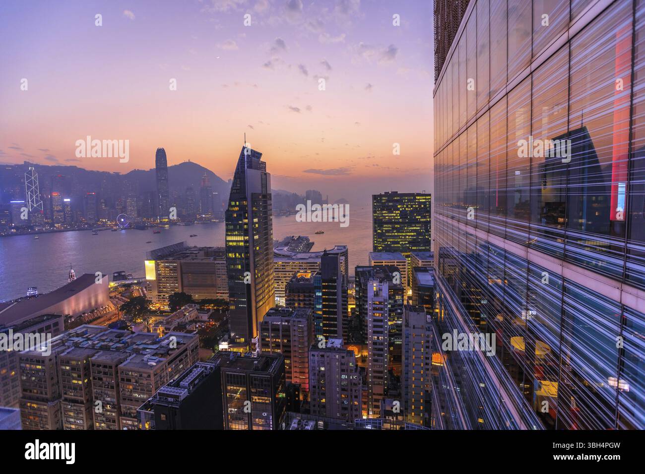 Spettacolare vista aerea del porto di Victoria, dei grattacieli e dello skyline di Hong Kong di notte. Lo skyline si riflette nella facciata di vetro di un edificio moderno Foto Stock