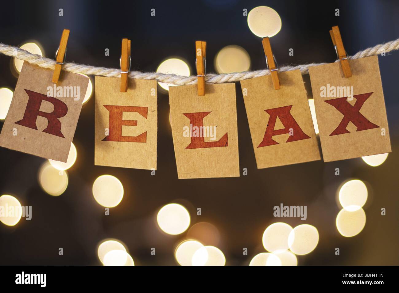 La parola RELAX è stampata su carte clothespin tagliate davanti a luci incandescenti sfocate Foto Stock