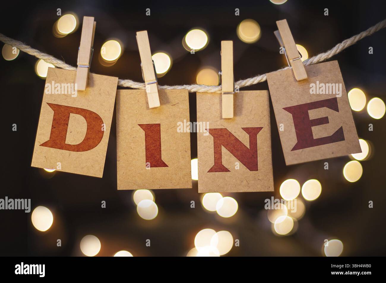 La parola "CENA" è stampata su carte clothespin tagliate davanti a luci incandescenti sfocate Foto Stock