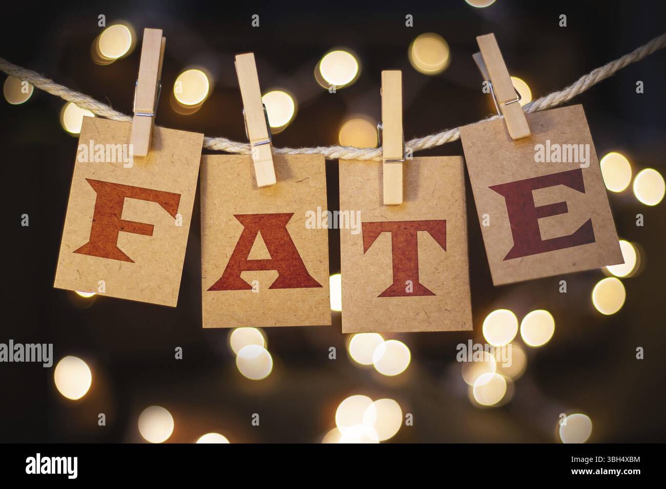 La parola FATE è stampata su carte clothespin tagliate davanti a luci incandescenti sfocate Foto Stock