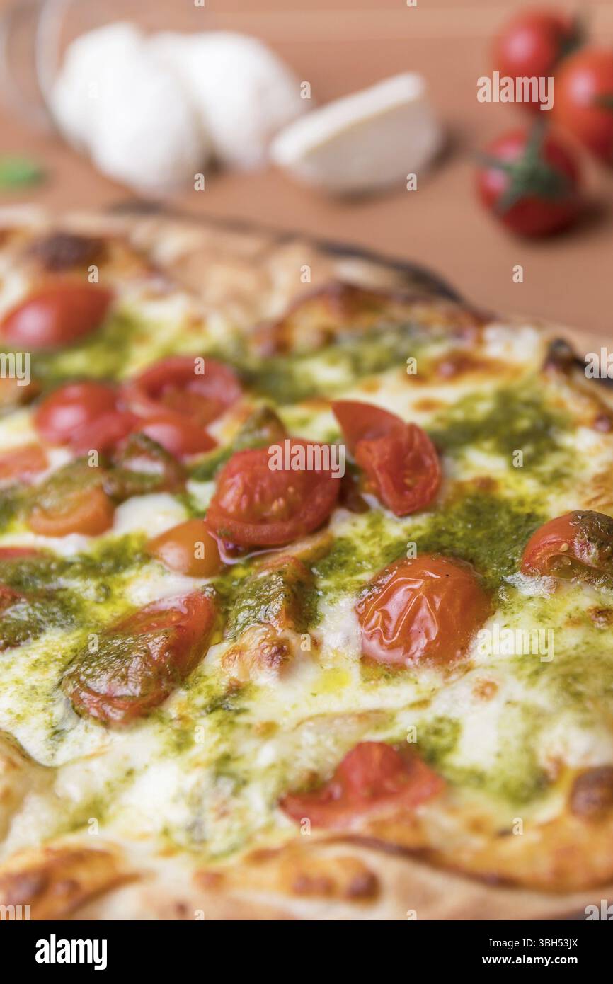 Pizza italiana con pomodori ciliegini, salsa al pesto basilico e mozzarella cotta nel forno a legna. Cucina italiana Foto Stock
