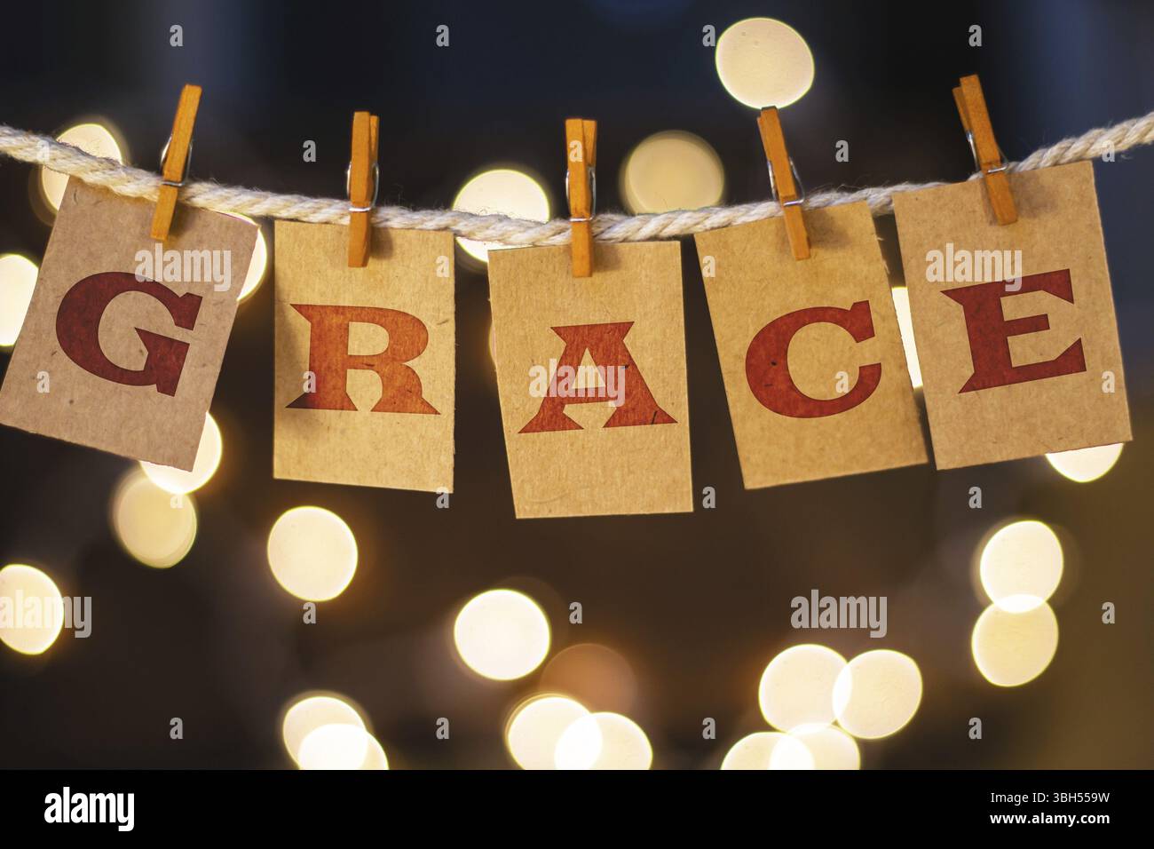 La parola GRACE è stampata su carte clothespin ritagliate davanti a luci incandescenti sfocate Foto Stock