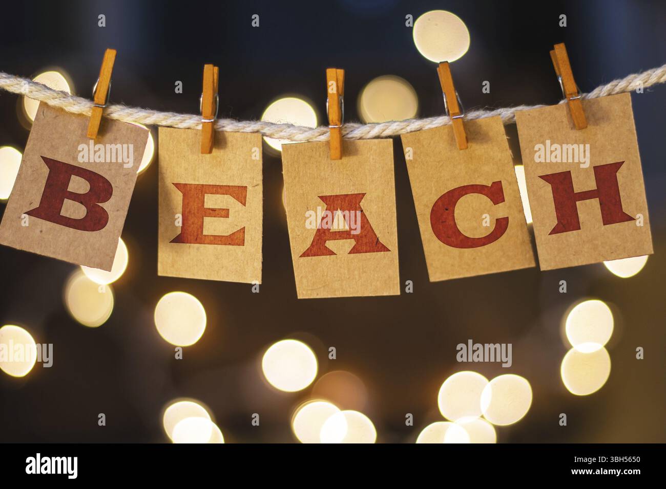 La parola BEACH è stampata su carte clothespin ritagliate davanti a luci incandescenti sfocate Foto Stock