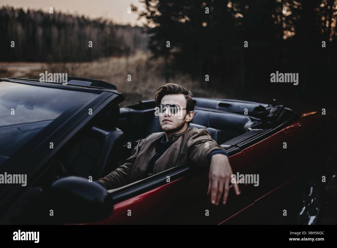 Persona a bordo di una cabriolet che indossa occhiali da sole, mostrando un'atmosfera rilassata al tramonto Foto Stock