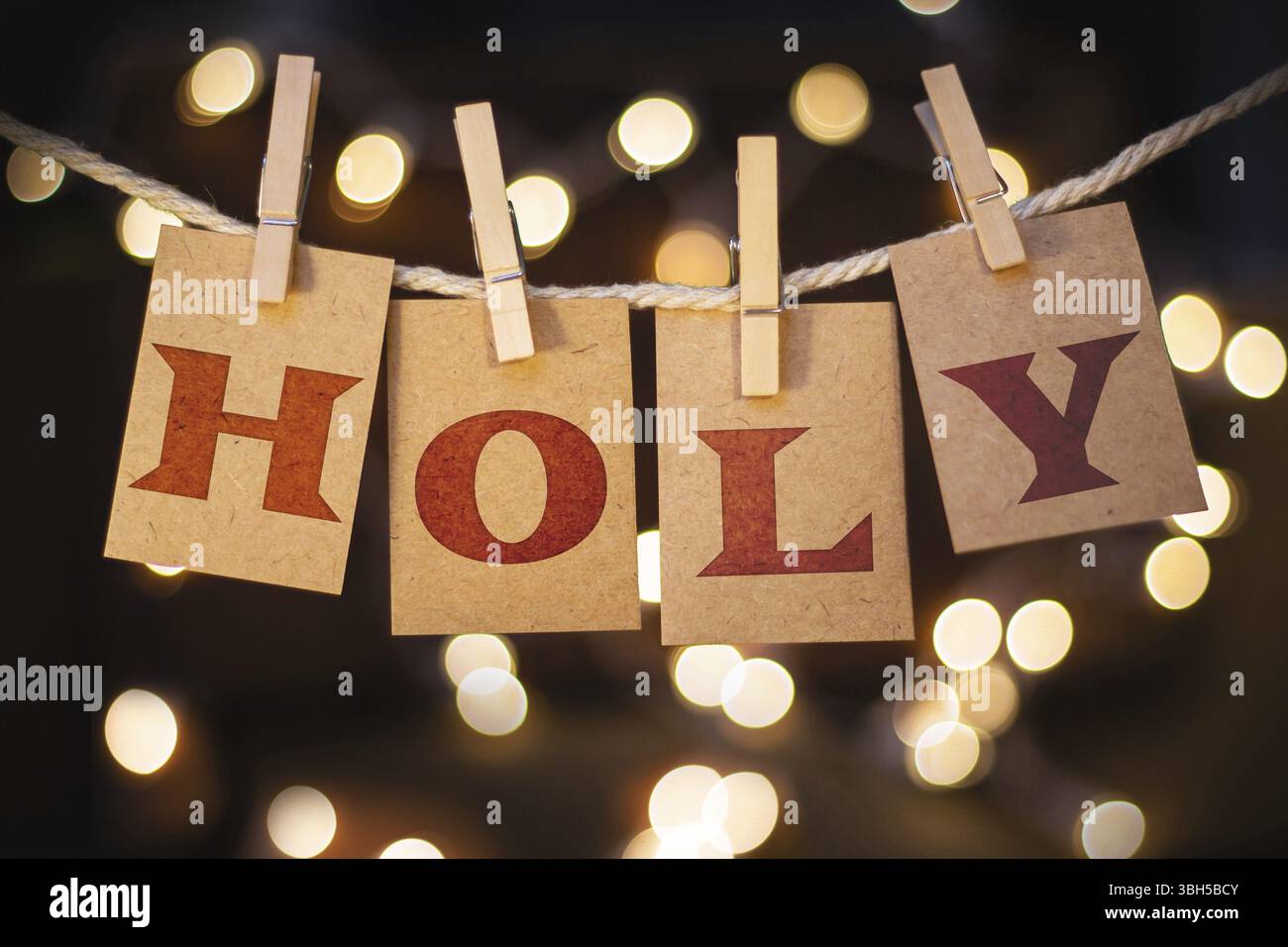 La parola "HOLY" è stata pronunciata sulle carte clothespin tagliate davanti a luci accese Foto Stock