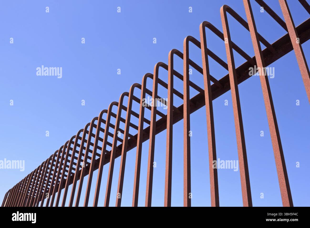 Frammento di recinzione con aste metalliche piegate contro un cielo blu Foto Stock