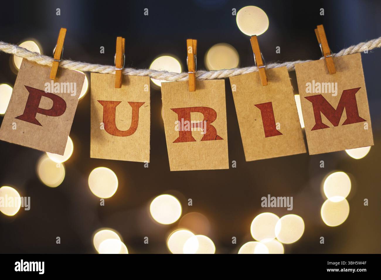 La parola PURIM è stampata su carte clothespin tagliate davanti a luci incandescenti sfocate Foto Stock