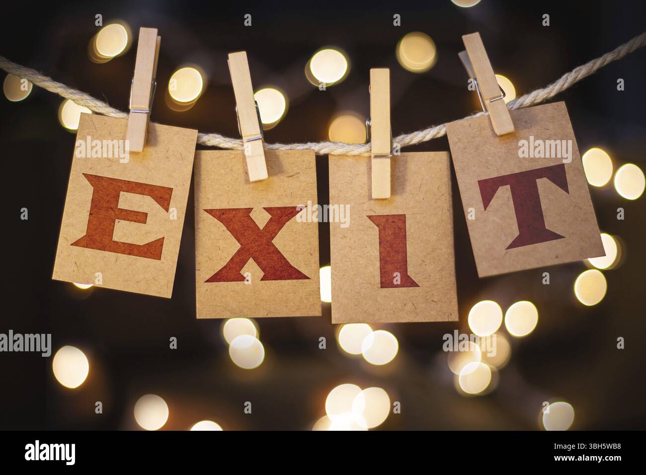 La parola "exit" è stampata sui biglietti ritagliati di clothespin davanti a luci incandescenti sfocate Foto Stock