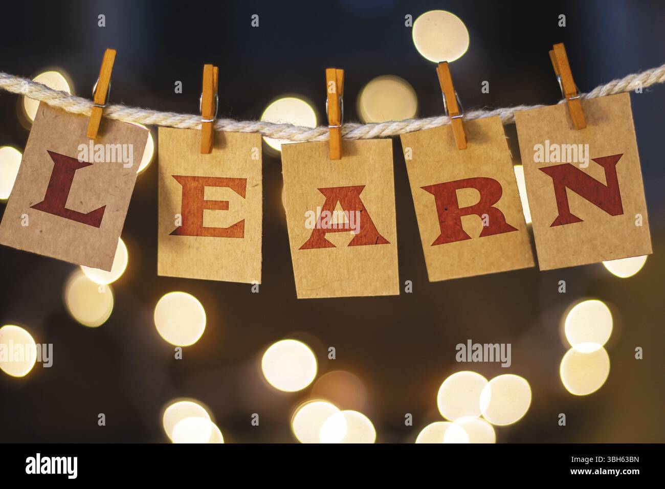 La parola "LEARN" è stampata su carte clothespin tagliate davanti a luci incandescenti sfocate Foto Stock