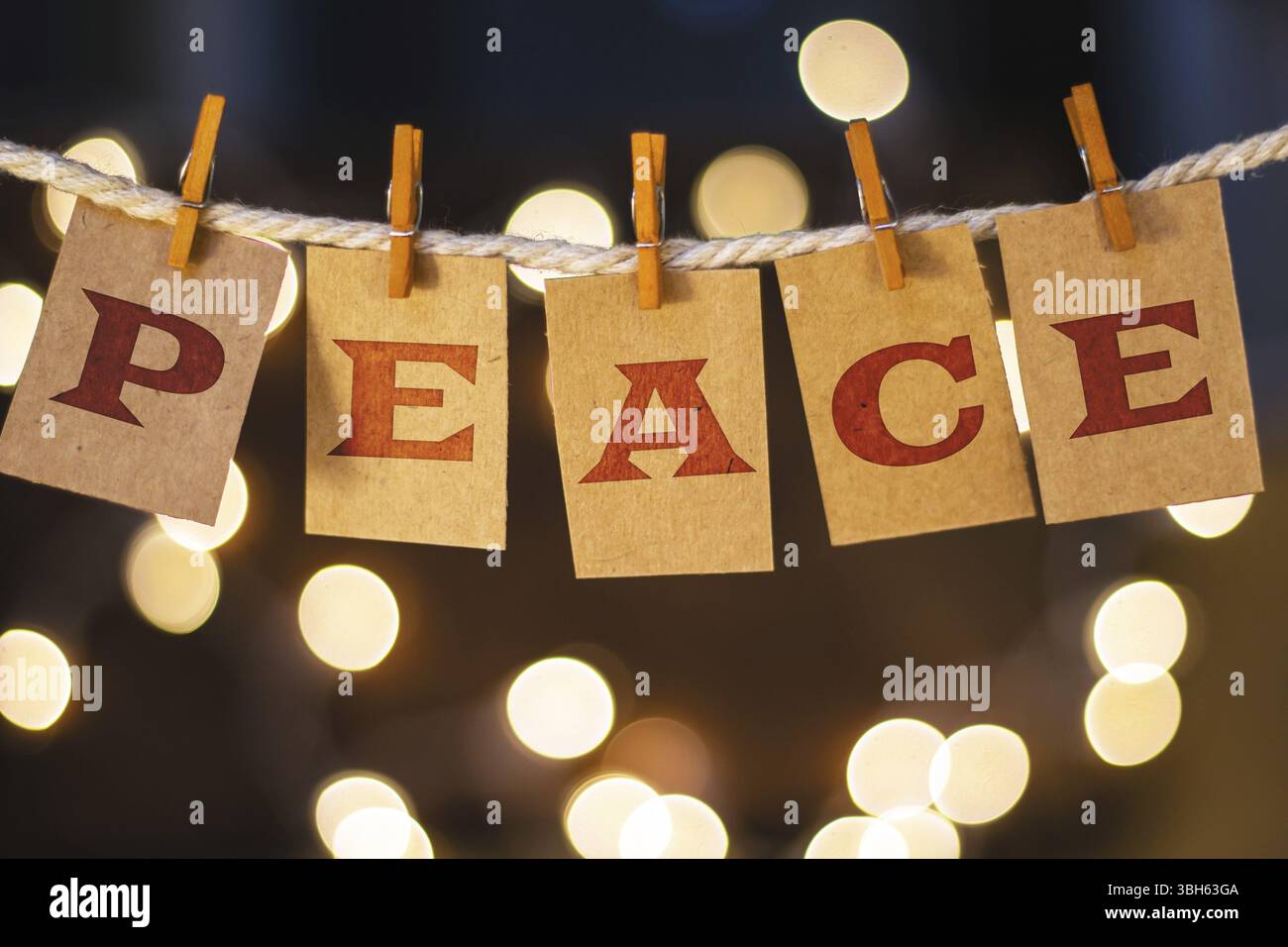 La parola PACE è stampata su carte ritagliate di clothespin davanti a luci incandescenti sfocate Foto Stock
