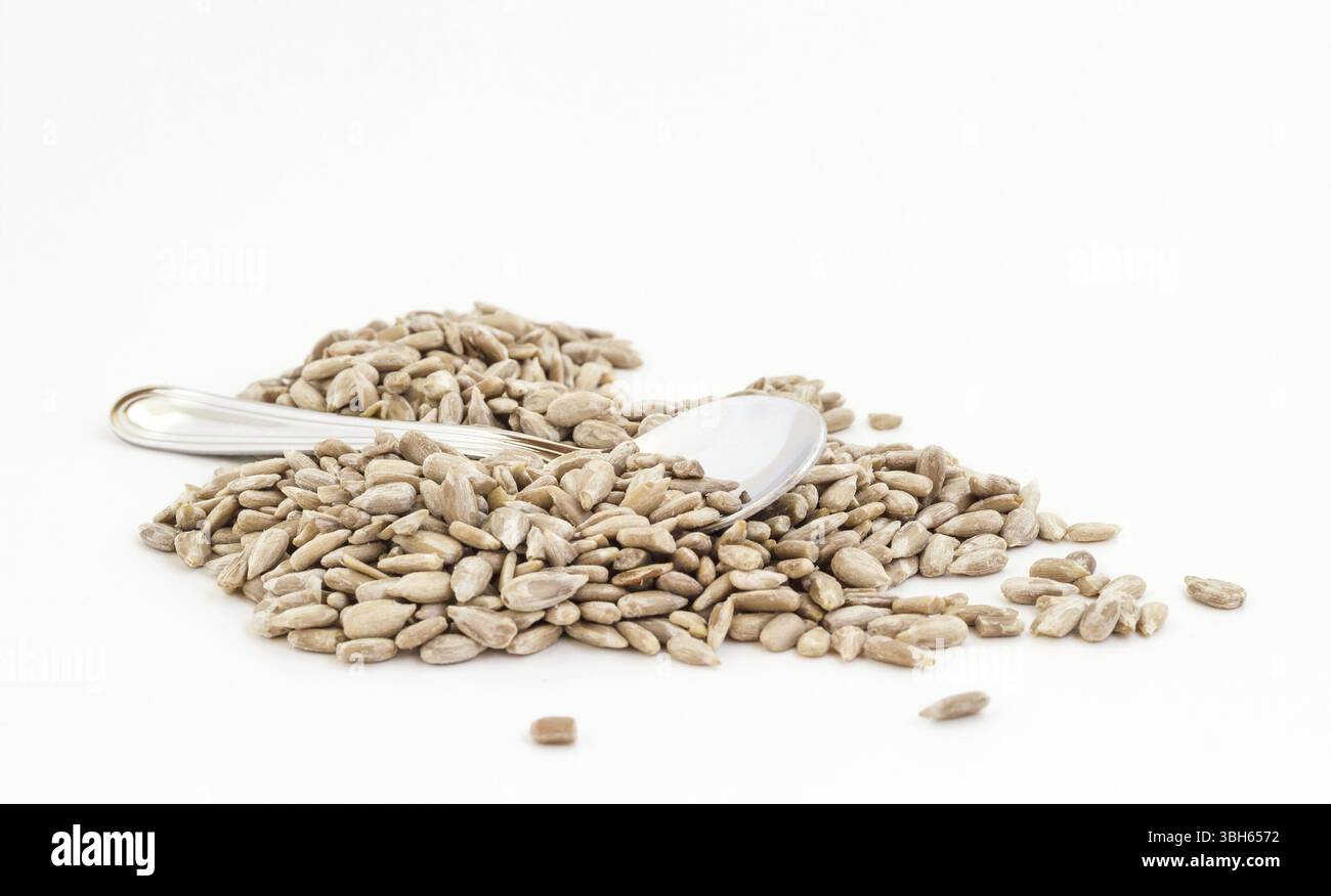 Semi di girasole sgusciati naturali con cucchiaio piccolo su sfondo bianco. Profondità di campo ridotta Foto Stock