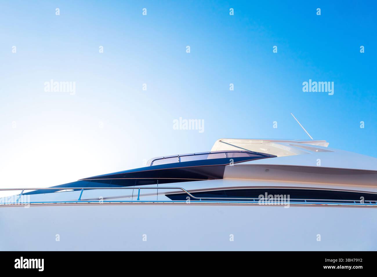 Lo scafo di un lussuoso yacht bianco a motore, con oblò sopra, contro il cielo blu e la luce del sole nell'angolo, vista dal basso. Foto Stock
