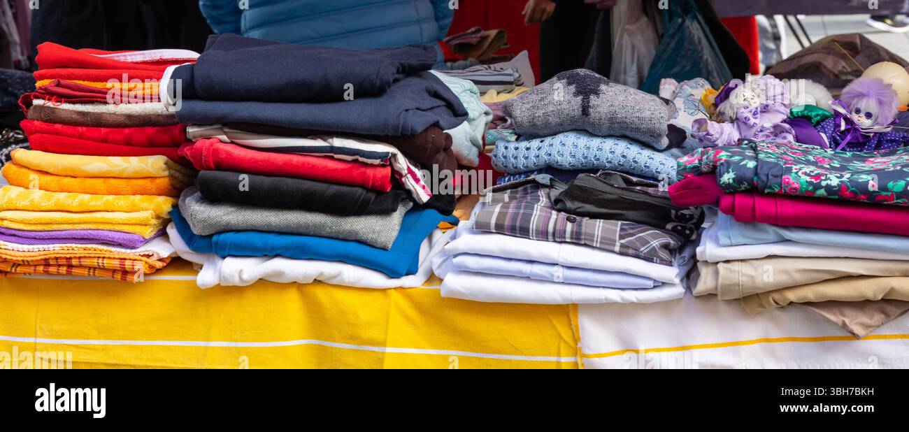 Una varietà di vecchi vestiti, saltatori e coperte offerti in un mercato delle pulci Foto Stock