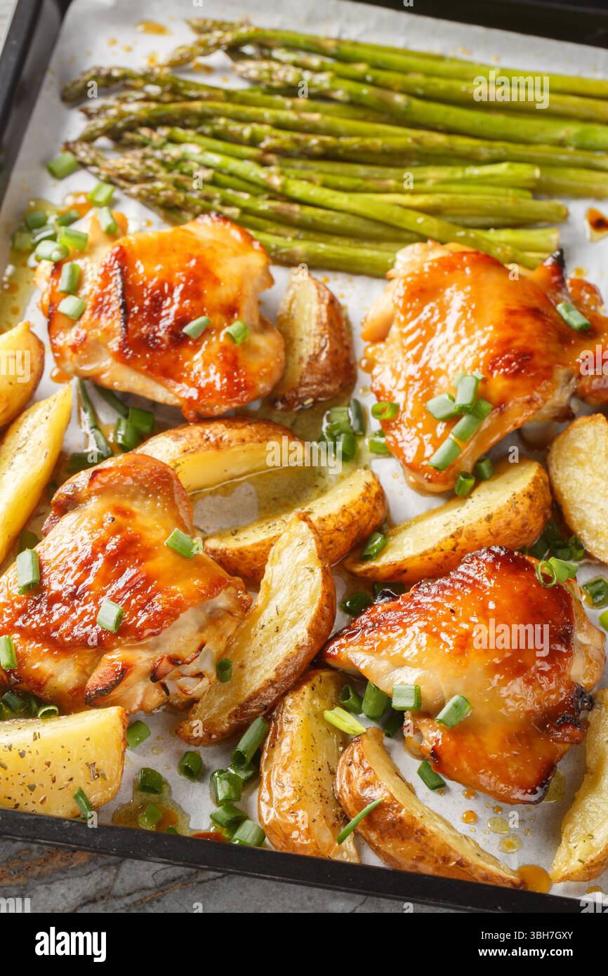 Cosce di pollo al forno con spicchi di patate e asparagi in primo piano su una teglia da forno sul tavolo. Verticale Foto Stock