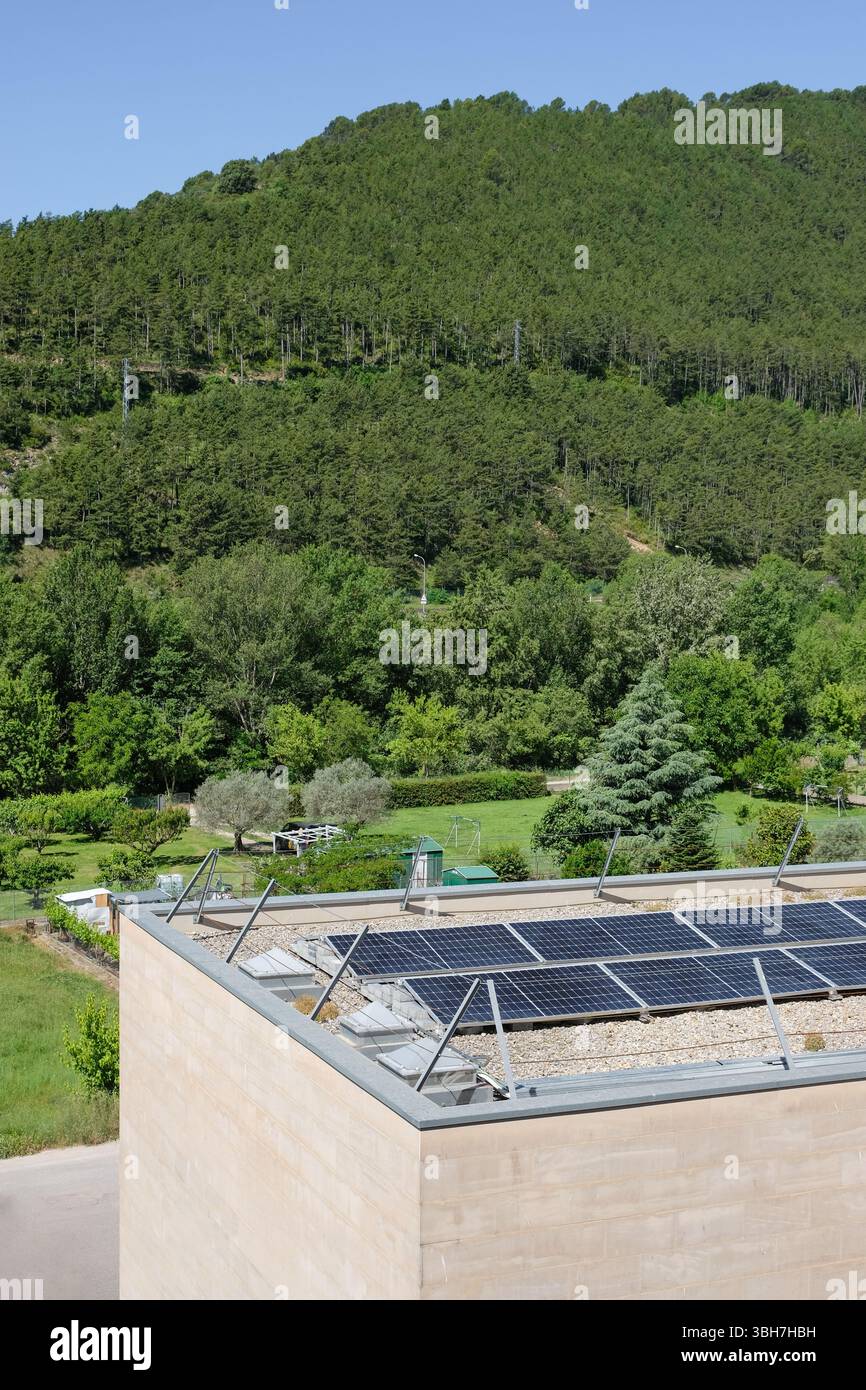 I pannelli solari su un moderno edificio a tetto piatto, circondato da lussureggianti boschi e montagne, illustrano l'energia rinnovabile. Copia spazio. Foto Stock