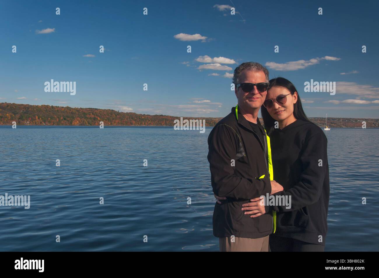 Un uomo birazziale e una donna che indossa occhiali da sole che si tengono in braccio davanti al lago Cayuga a trumansburg, New york, in autunno. Foto Stock