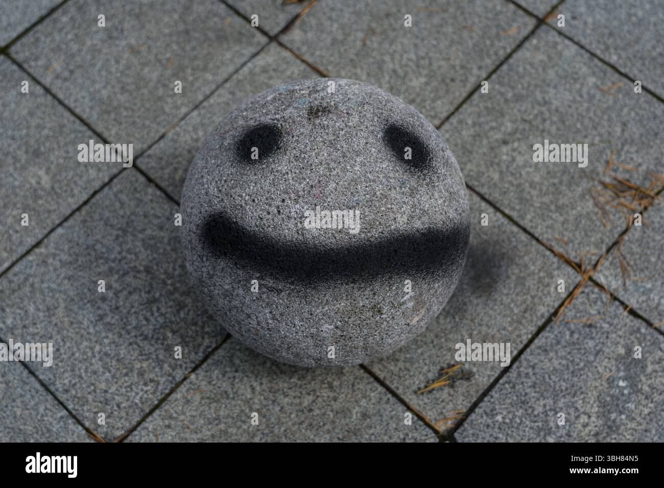 Una sfera di pietra con una faccia dipinta su di essa. Faccia Smiley Foto Stock
