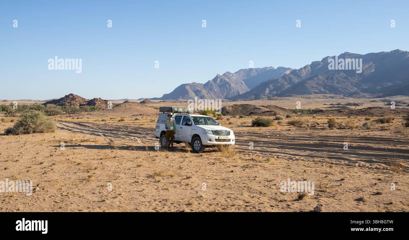 Turista con auto fuoristrada su una pista sabbiosa, formazione rocciosa, Brandberg, Damaraland, Namibia, Africa Foto Stock