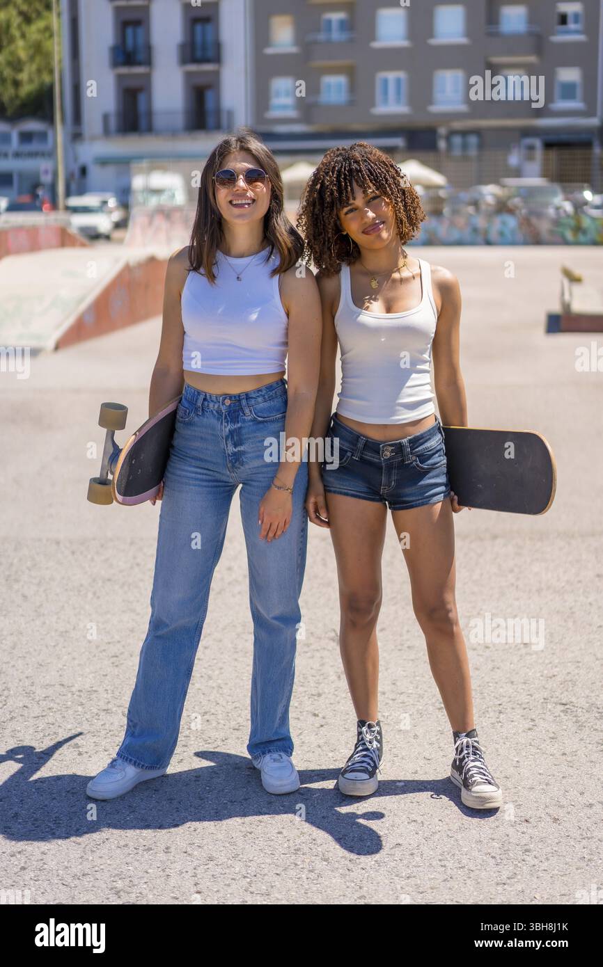 Due giovani pattinatrici in posa con i loro skateboard in un vivace skate Park, godendosi la giornata di sole e abbracciando il loro stile di vita attivo Foto Stock