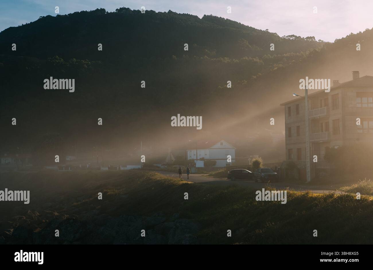 Pellegrini con zaini che camminano lungo il cammino durante la mattina presto sul famoso cammino di Santiago illuminato da magici raggi dell'alba e dal peac Foto Stock