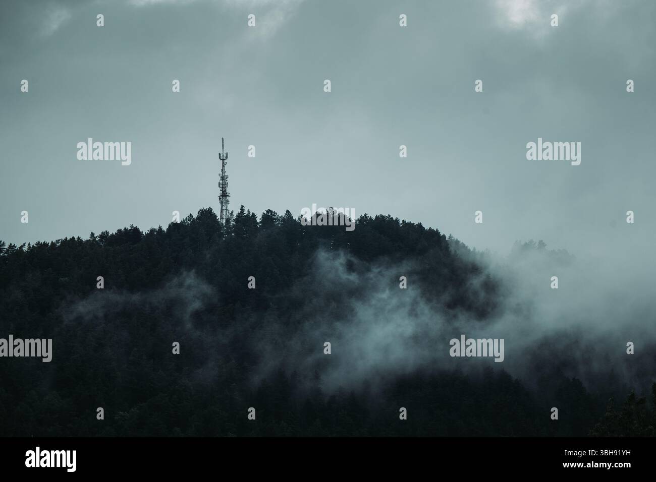 Foto Moody del trasmettitore sulla cima della collina con nebbia post pioggia e clima nuvoloso Foto Stock