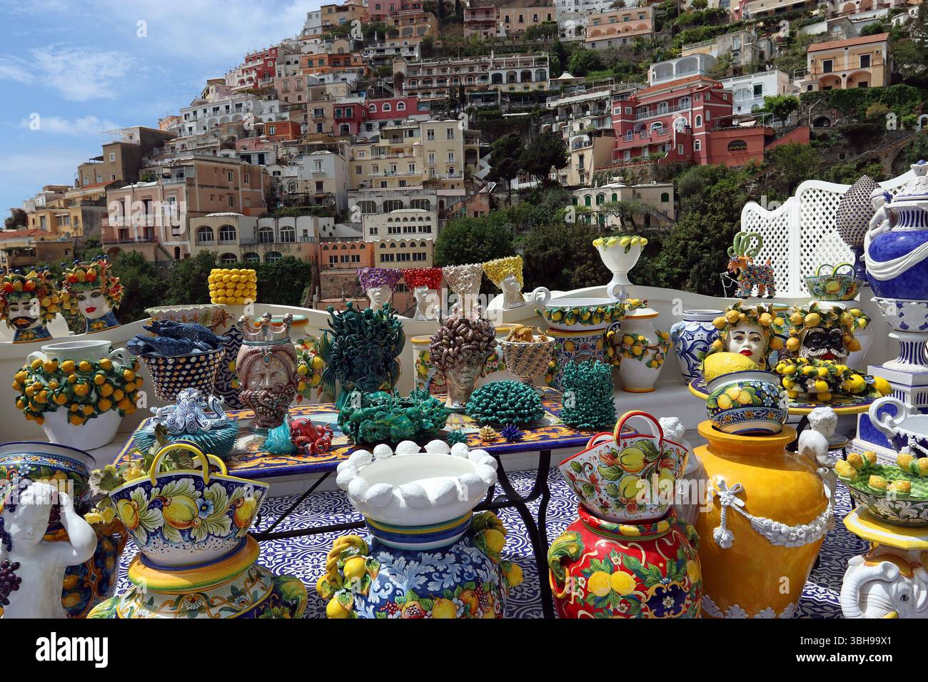 Esposizione all'aperto di colorate ceramiche fatte a mano a Positano con uno sfondo di case costruite sopra la città. Maggio '25 Costiera Amalfitana, Campania Italia Foto Stock