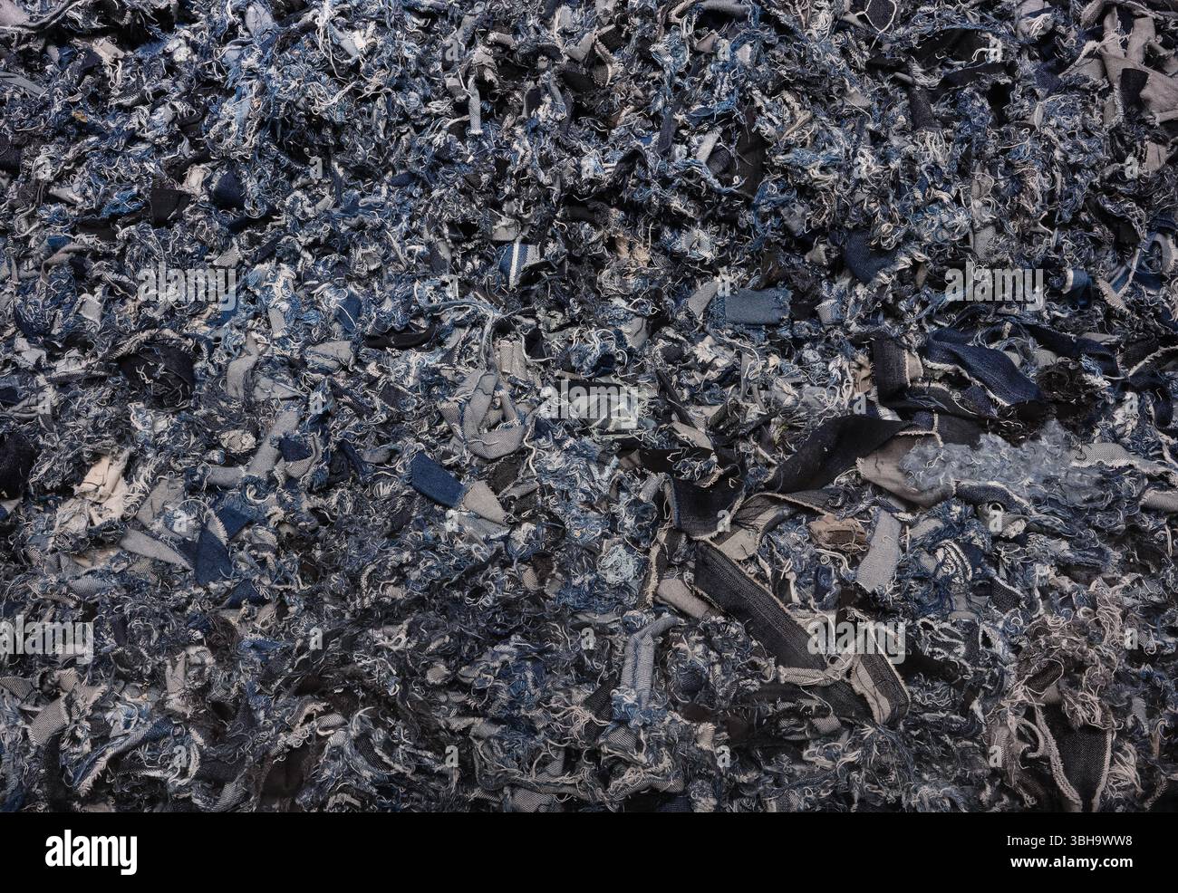 Primo piano sull'intricata trama del tessuto in denim triturato utilizzato come jeans riciclati, sottolineando la moda eco-consapevole e le pratiche tessili sostenibili Foto Stock