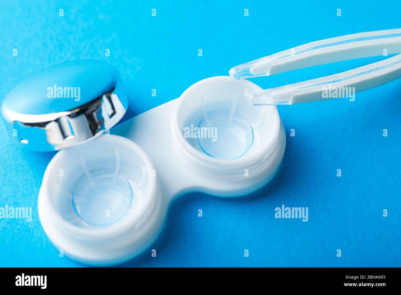 Lenti a contatto nella custodia e pinzette su sfondo blu, sopra la vista Foto Stock