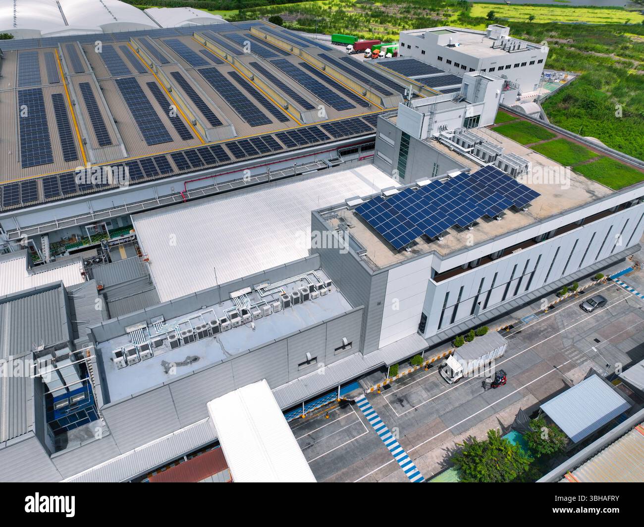 Magazzino a energia solare con autocarri nelle banchine di carico. Logistica ecocompatibile e trasporto merci efficiente. Pannelli solari Foto Stock